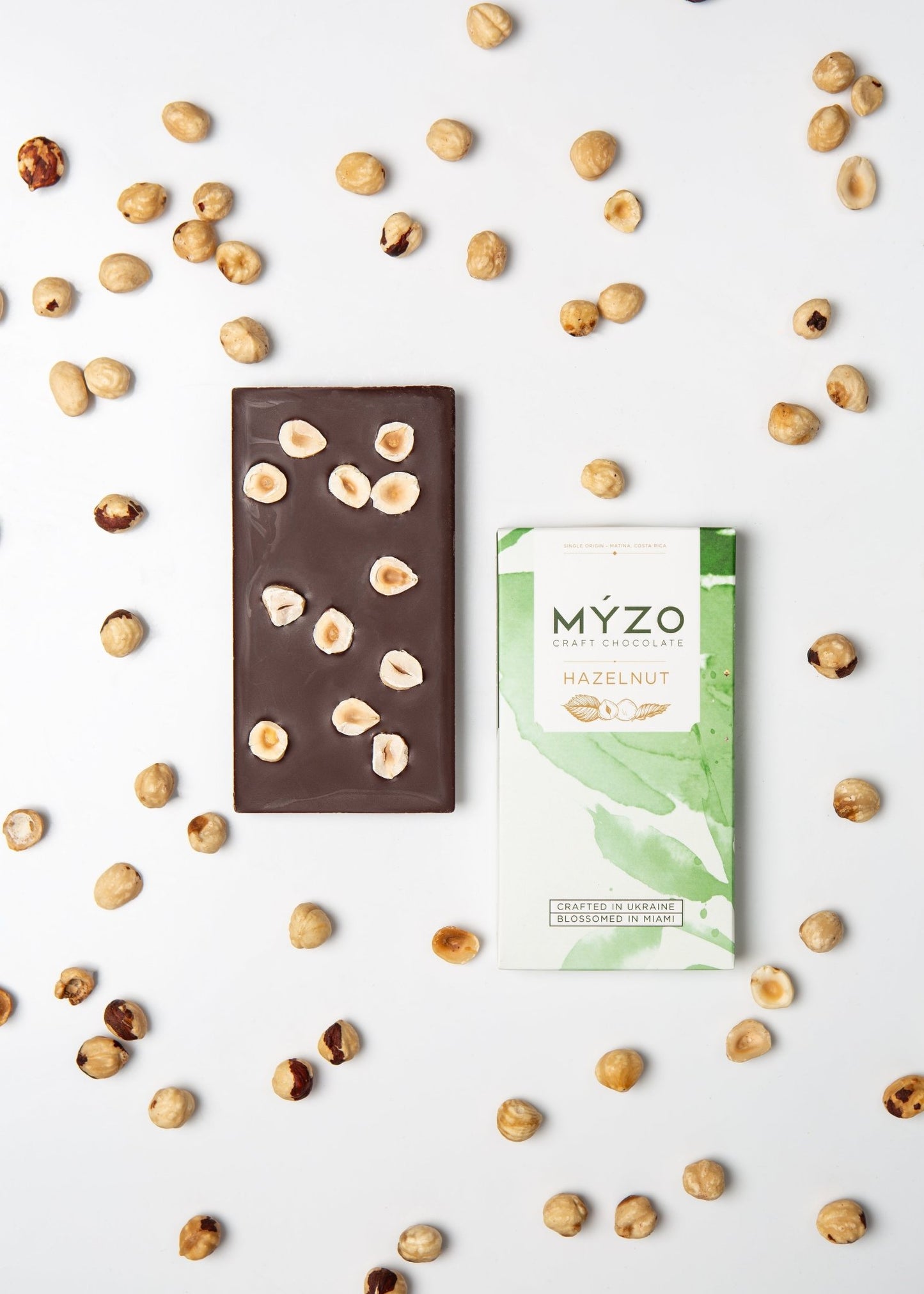Flat lay of MYZO Hazelnut Dark Chocolate bar with packaging and roasted hazelnuts