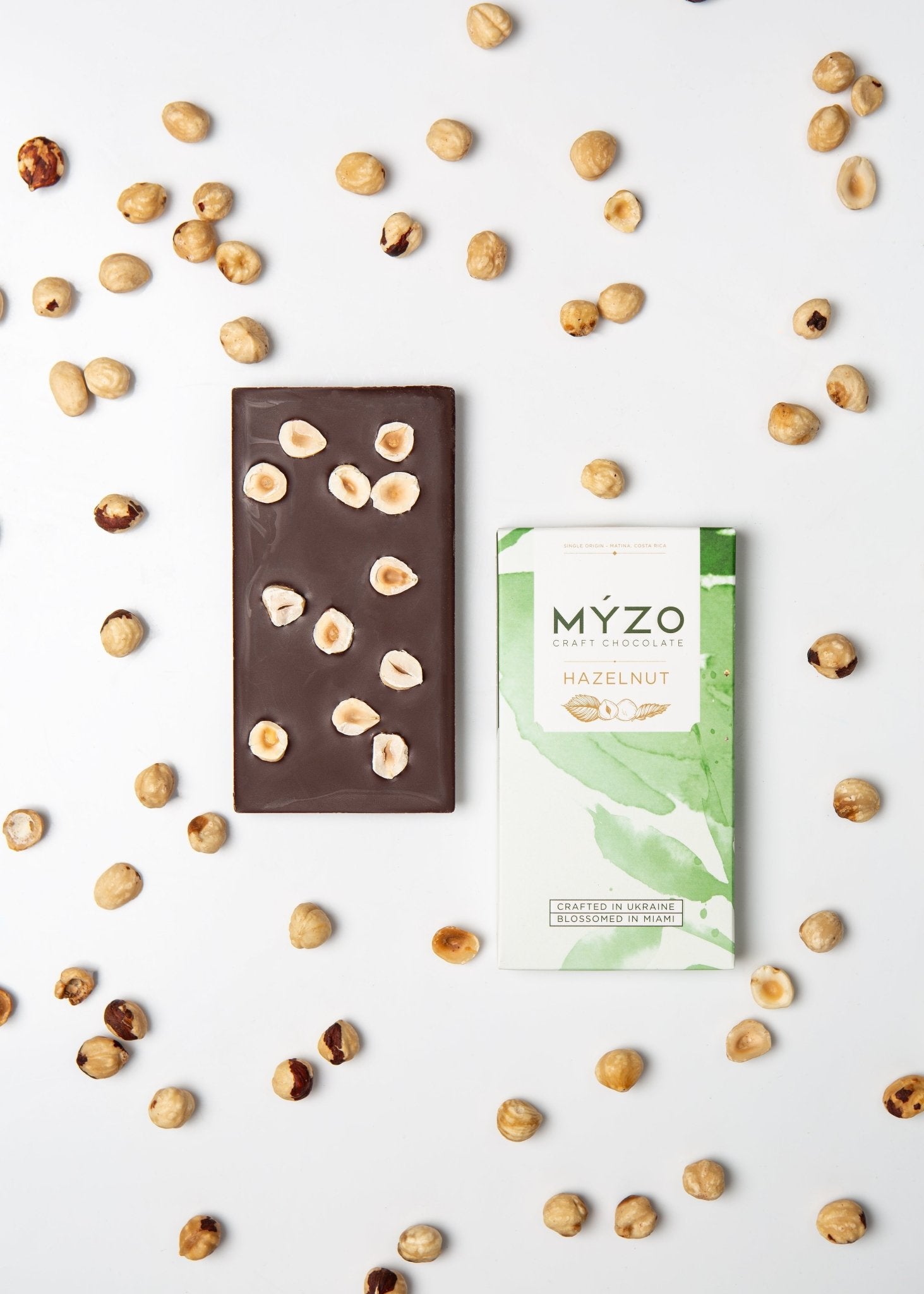 Flat lay of MYZO Hazelnut Dark Chocolate bar with packaging and roasted hazelnuts