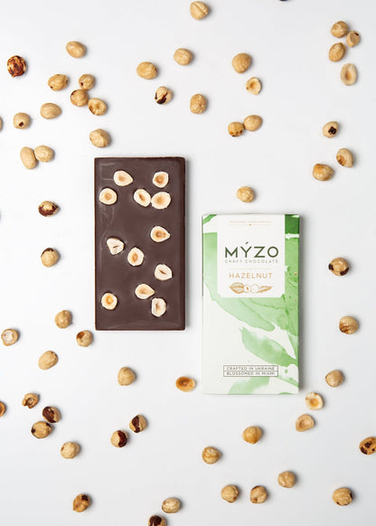 Flat lay of MYZO Hazelnut Dark Chocolate bar with packaging and roasted hazelnuts