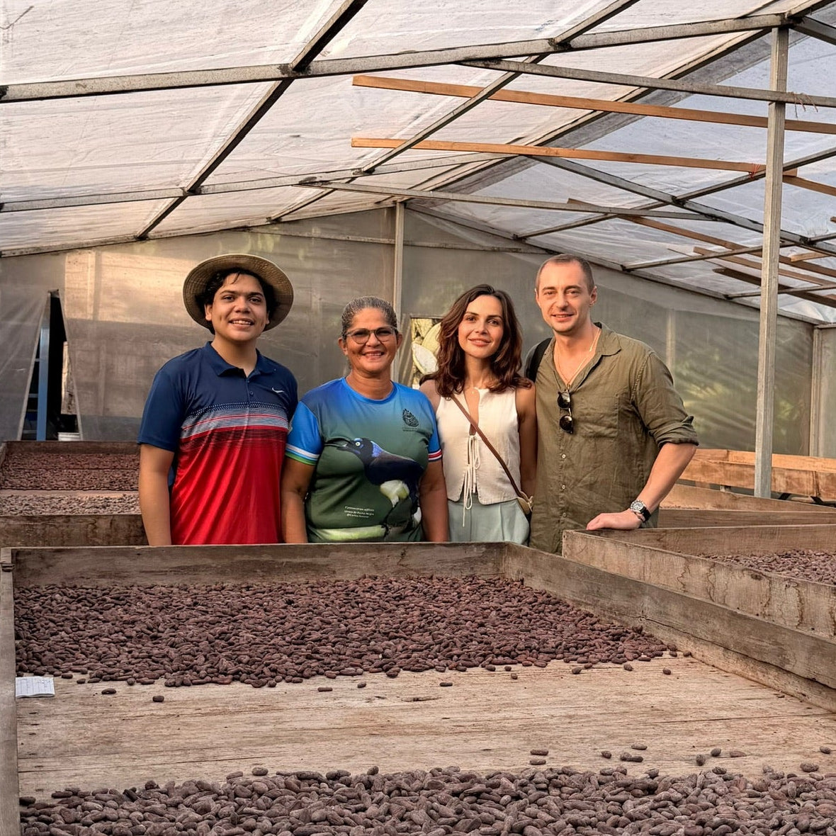 Four people standing inside a greenhouse with rows of drying cacao beans.
