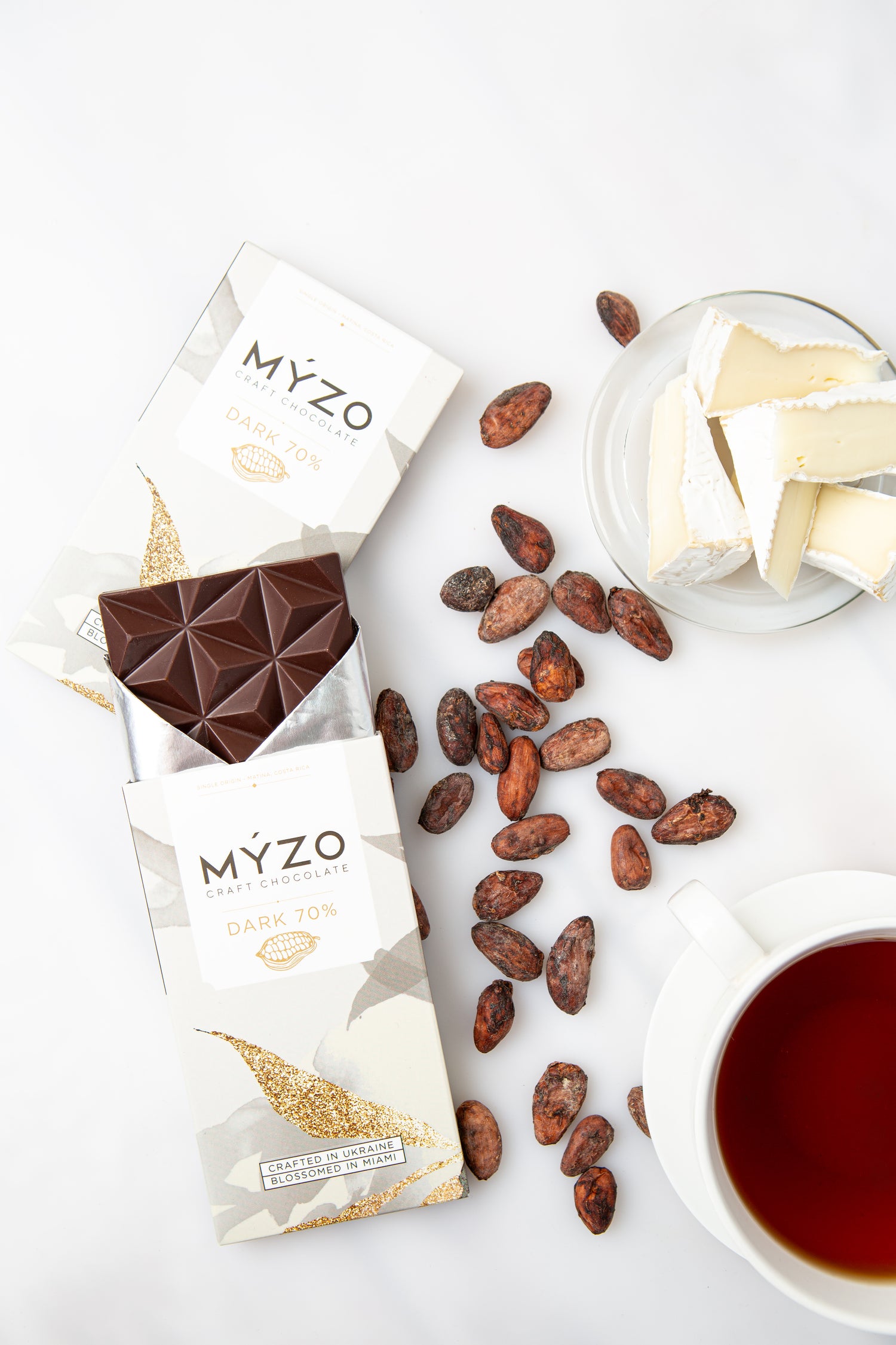 MYZO chocolate bar packaging with cocoa beans, a glass of milk, and a cup of tea on a white surface.